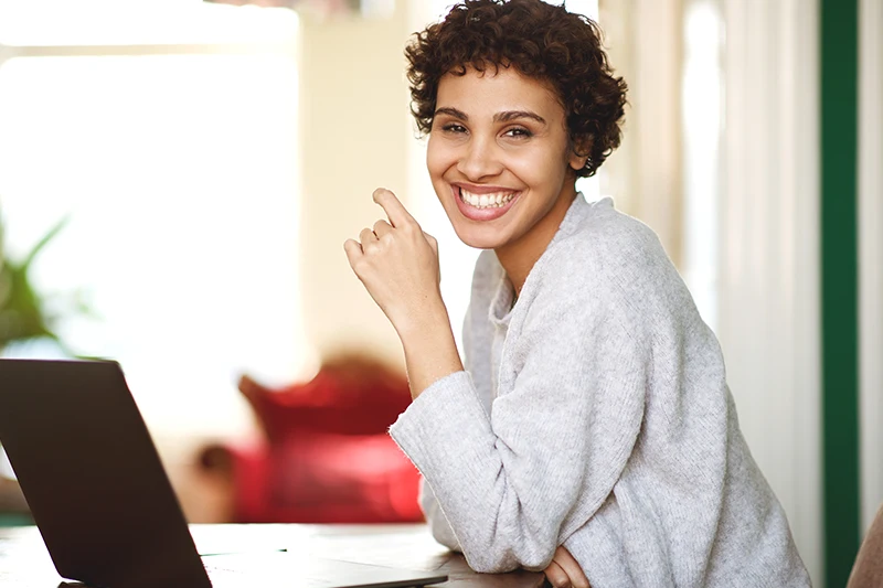 Mulher sorrindo de forma confiante em frente a um notebook, demonstrando a total discrição ao usar o aparelho auditivo 100% invisível Lyric.